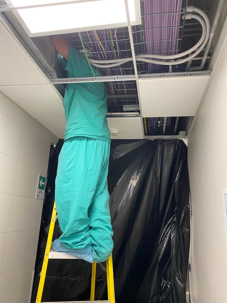 Técnico de Redelectric trabajando sobre cielo falso en un pasillo de recinto clínico, con protección de la zona